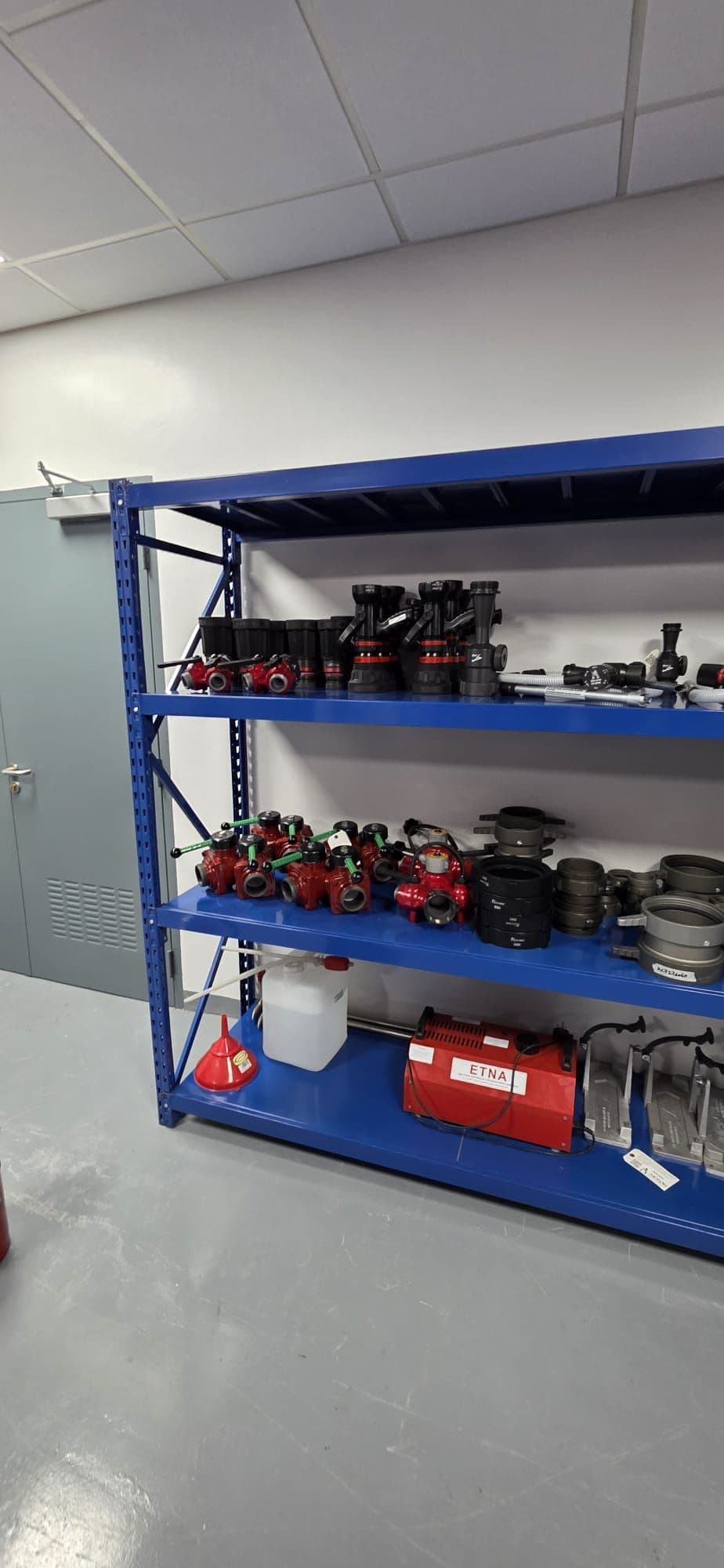 Small equipment, harnesses and hand tools sorted into bins on blue shelving.