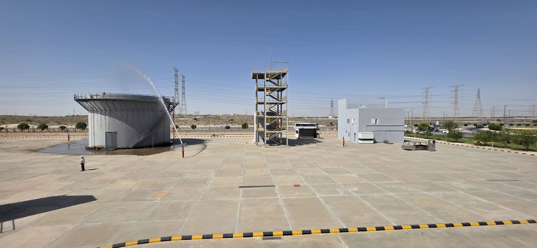 A storage-tank prop with water running over its rim, the drill tower standing behind it.