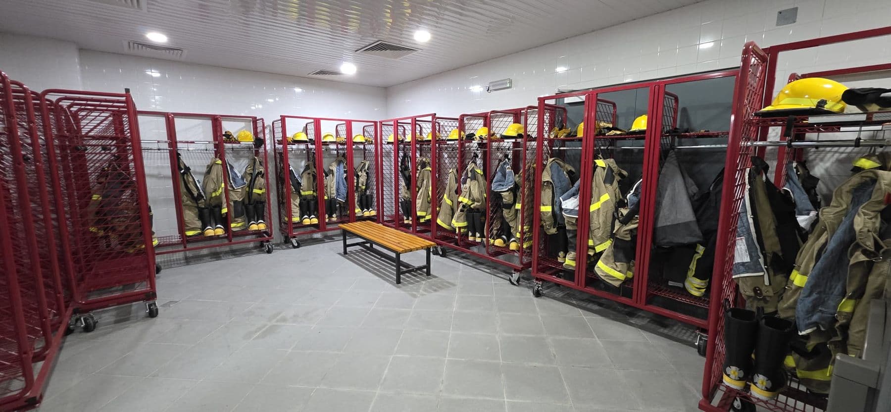 Turnout coats, trousers and helmets hanging on red racks along both sides of the gear store.